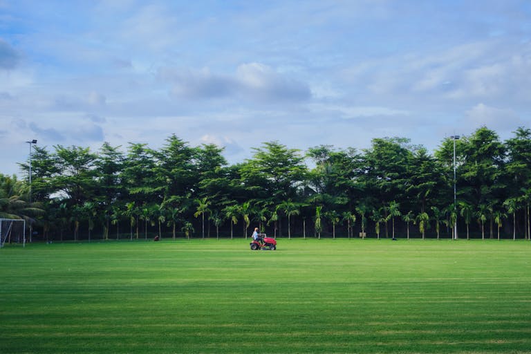 A man mowing the grass on a pristine golf course in Dhaka, Bangladesh, under a clear summer sky.