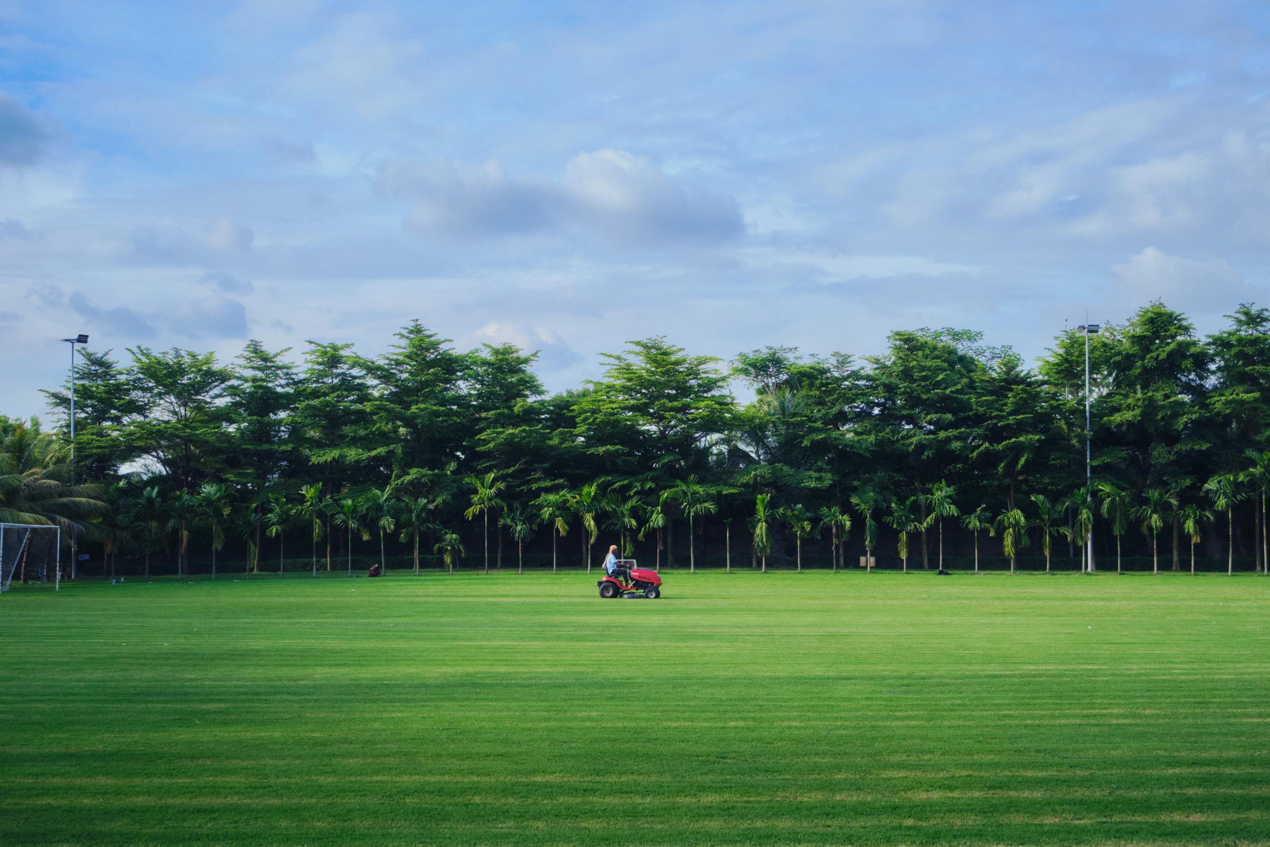 A man mowing the grass on a pristine golf course in Dhaka, Bangladesh, under a clear summer sky.